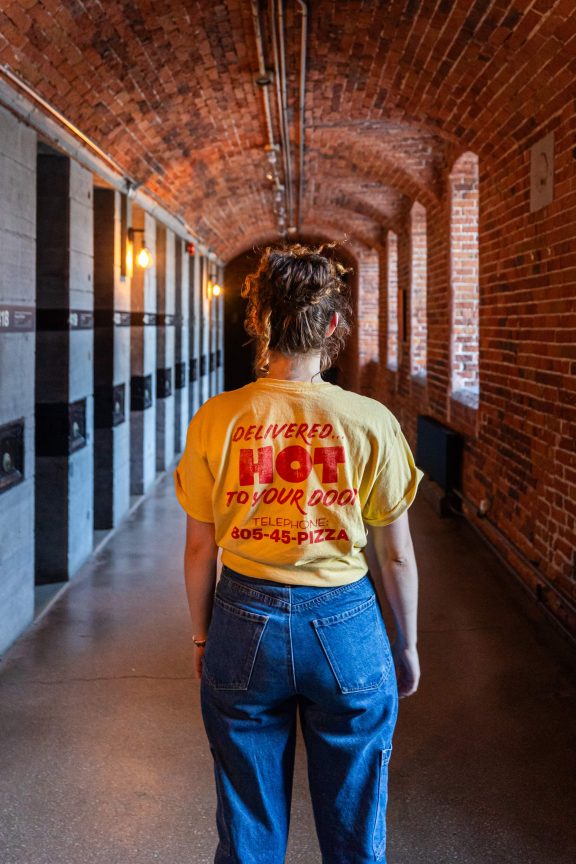 Woman with a yellow t-shirt in a red brick corridor of the Saintlo Ottawa Jail Hostel.