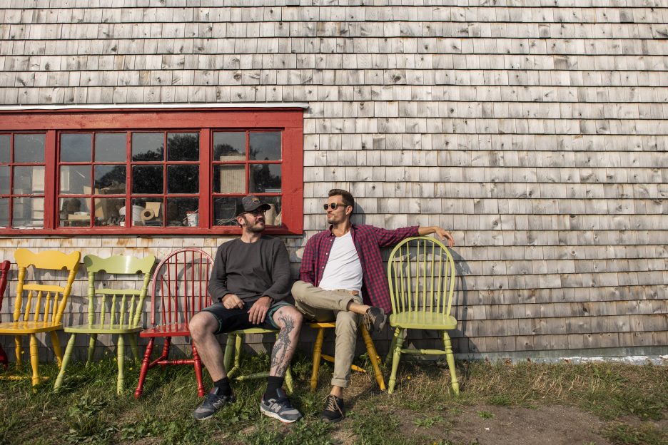 Deux hommes sur des chaises multucolores devant un bâtiment en bois