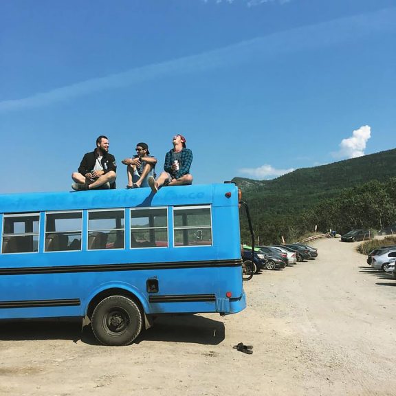 Three people sitting on the roof of a blue bus