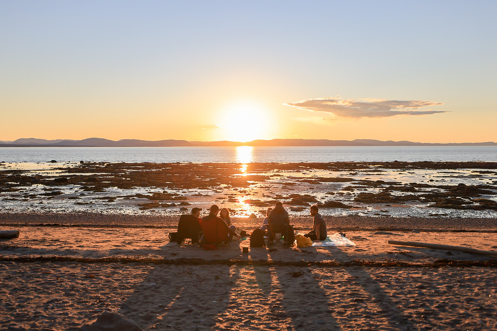 Groupe de gens au bord de l'eau devant un coucher de soleil