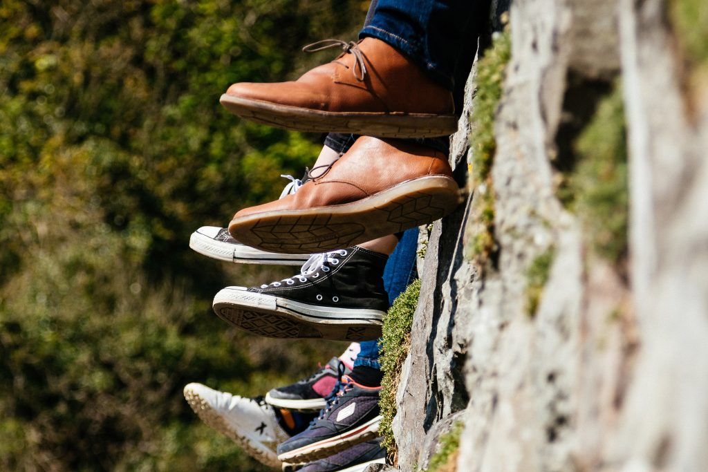 Many shoes of people seating on a wall