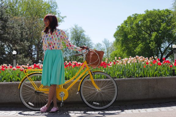 Une personne de dos, tenant un vélo, fleurs roses