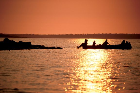 Three people in canoes at sunset