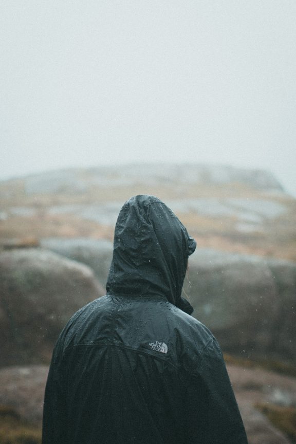 A person from behind in a raincoat, in front of a landscape