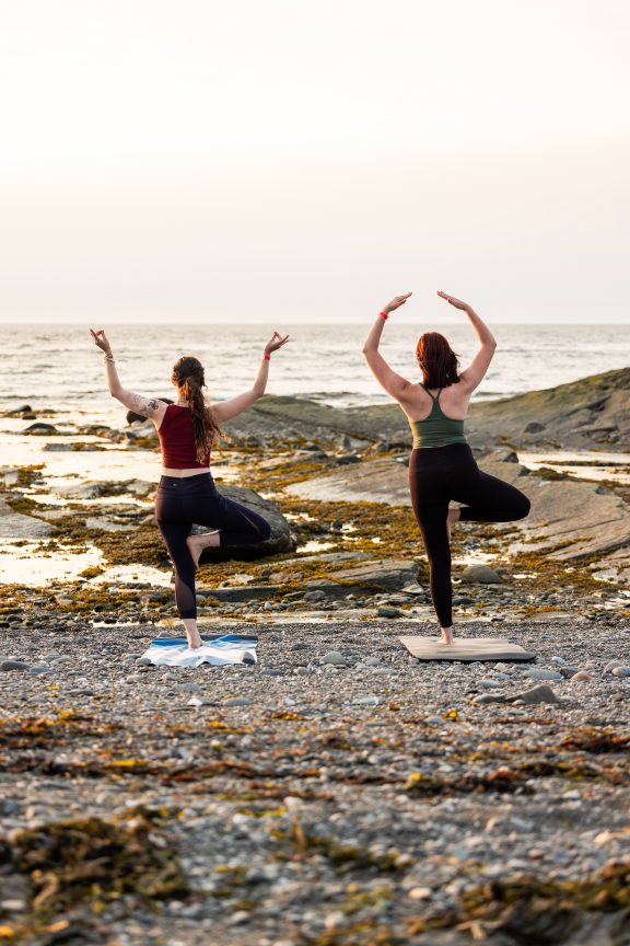 Two women do yoga in front of the sea, at the Sea Shack